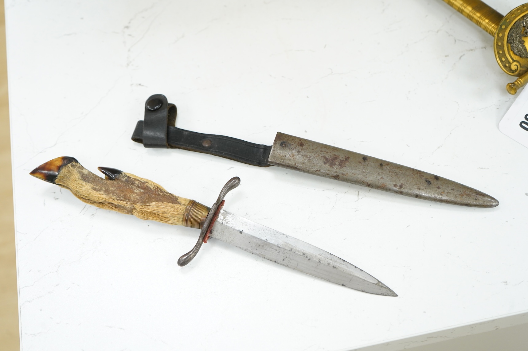 A First World War German Deer Hoof Fighting Knife, with a deer’s hoof grip, brass ferrell and steel cross guard, in original steel scabbard with leather belt loop mount, single edged blade with makers mark to one side; M